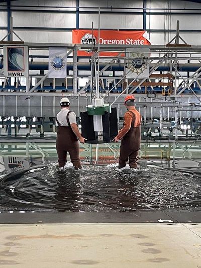 Tow people moving a device into a water bat in an indoor testing facility.