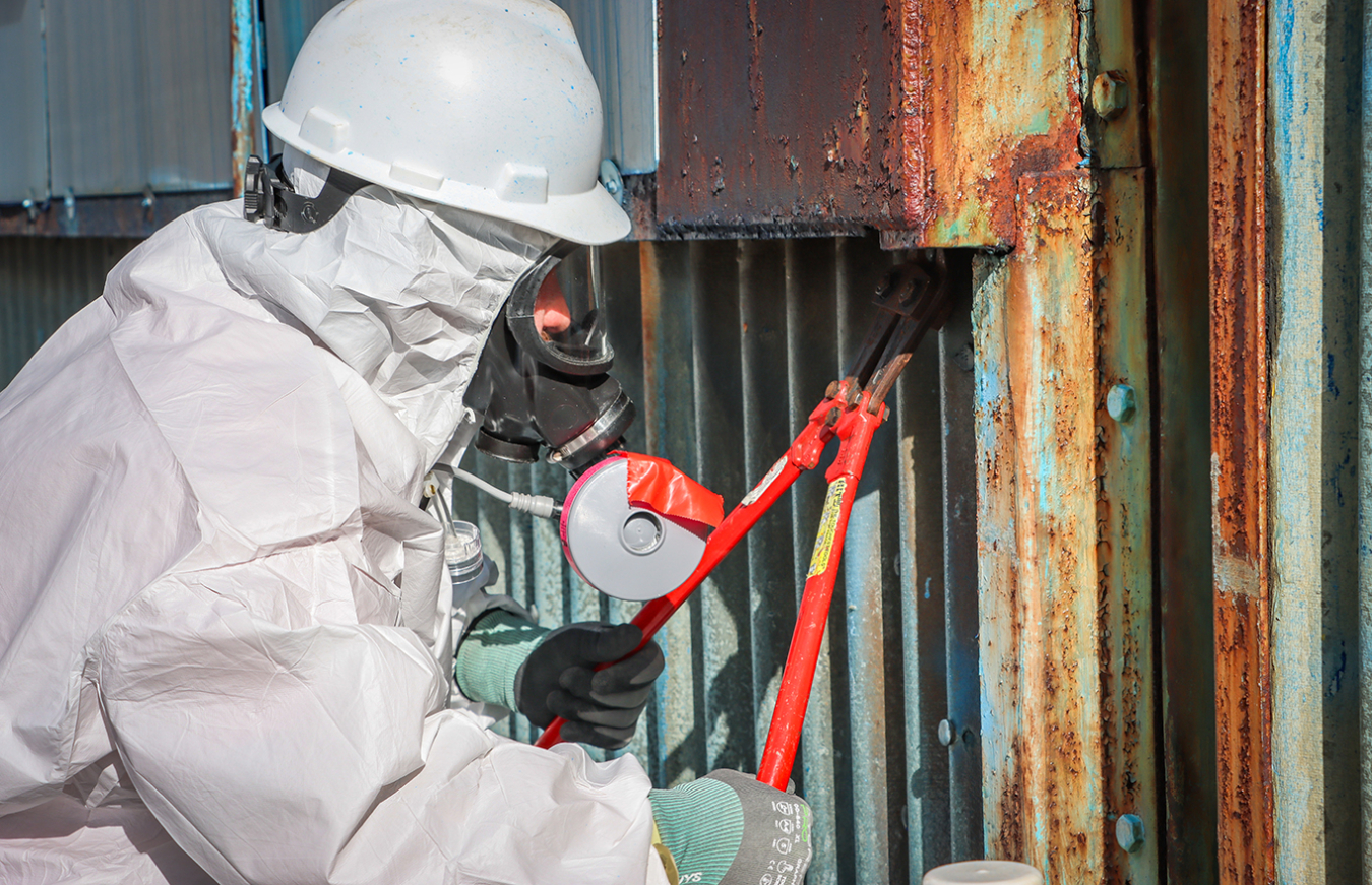 Employee in protective gear uses pliers on the outside of a building