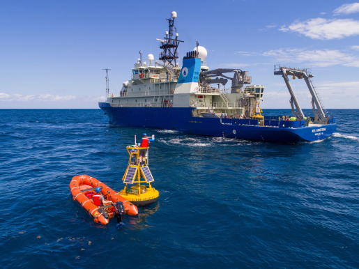 A weather buoy in the ocean with research boat in the background