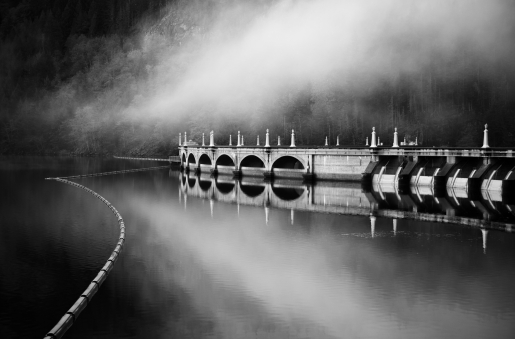 Black and white photo of a dam with clouds above it